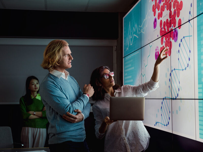 Scientists looking at a screen displaying animal cells and a dna double helix