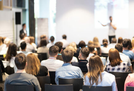 Room full of seated people listening to someone speak