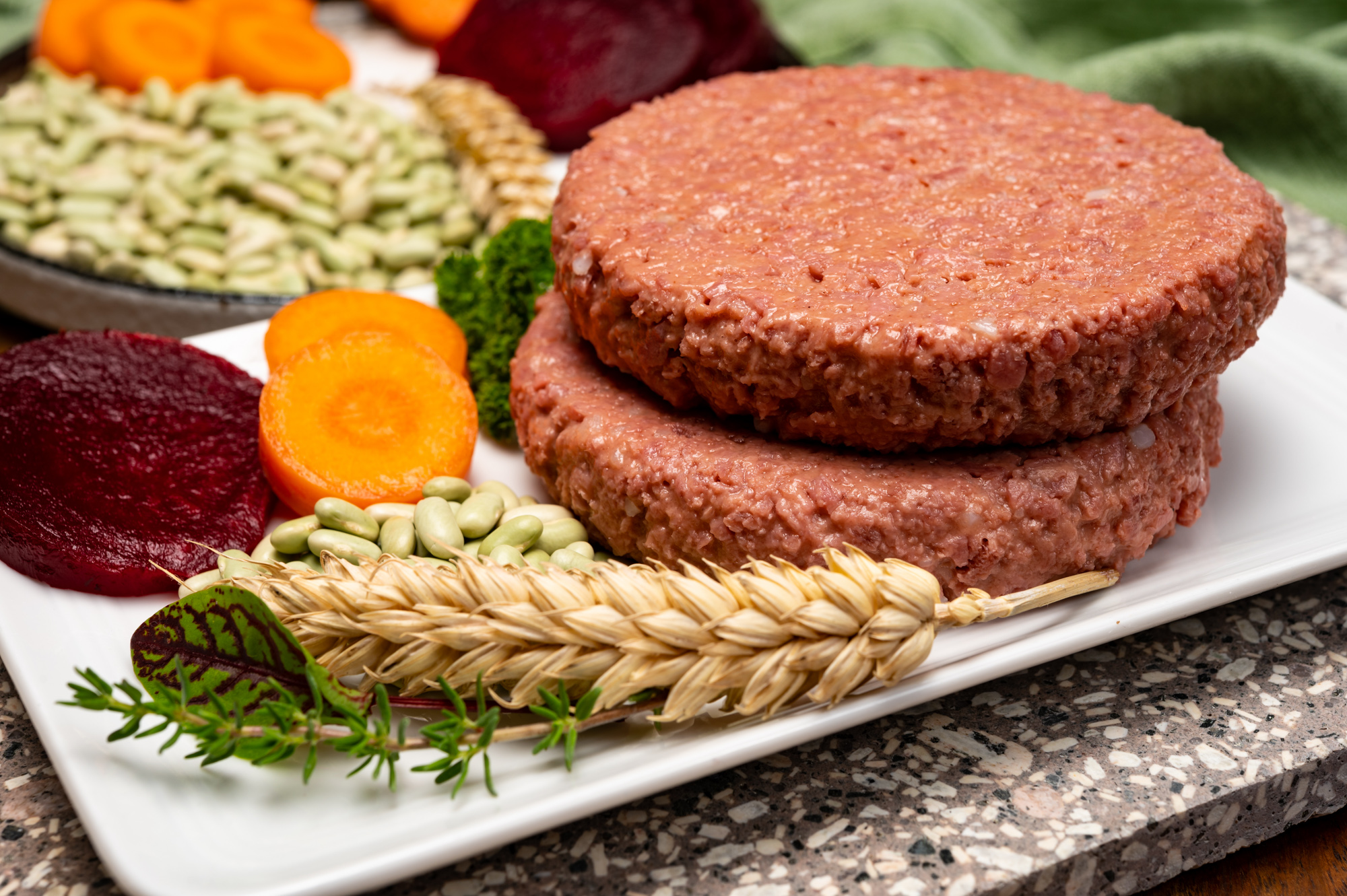 Deep dive: plant-based meat end product formulation and manufacturing 1 Plant based soy protein burger patties on a white plate next to wheat, legumes, carrots and beets